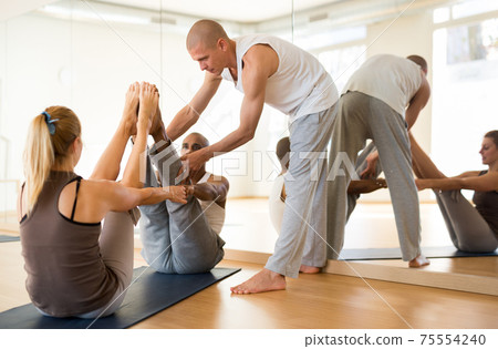 Couple practicing partner yoga position during training with instructor 75554240