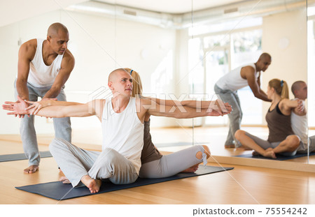 Sporty adult concentrated females and males doing stretching workout in pairs during group training Sporty adult concentrated females and males doing stretching workout in pairs during group training 75554242
