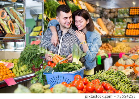 Young cheerful couple choosing vegetables in grocery shop Young cheerful couple choosing vegetables in grocery shop 75554255