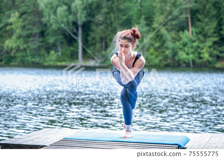Young yogi  girl  practicing yoga, standing in Eagle pose, Garudasana exercise on the lake. Concept of healthy life and natural balance 75555775