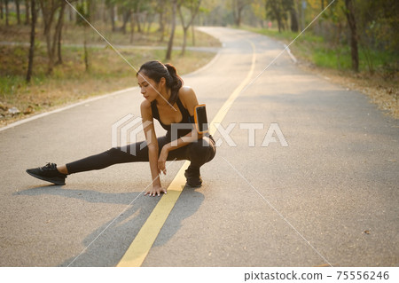 Sporty woman stretching her legs muscles before running. Sporty woman stretching her legs muscles before running. 75556246