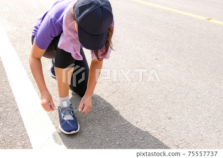 Active healthy woman tying running shoes,  jogging runner healthcare and well being concept. 75557737