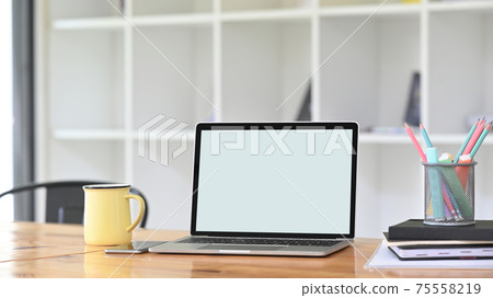 A comfortable workspace is surrounding by a white blank screen computer laptop and office equipment. A comfortable workspace is surrounding by a white blank screen computer laptop and office equipment. 75558219