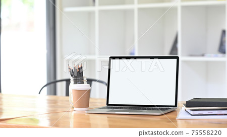 A comfortable workspace is surrounding by a white blank screen computer laptop and office equipment. A comfortable workspace is surrounding by a white blank screen computer laptop and office equipment. 75558220