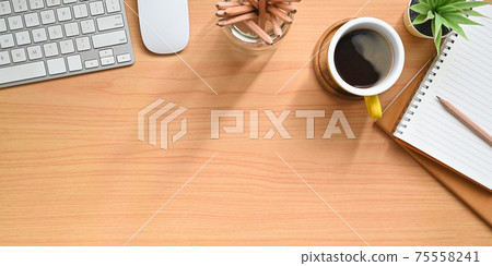 A wooden workplace is surrounding by a coffee cup and personal equipment. 75558241
