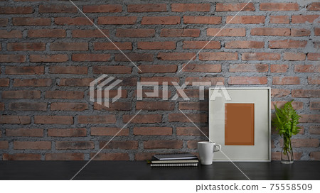 Photo of black working desk along with book, notebook, picture frame, potted plant and coffee cup putting together on it with brick wall as background. Orderly workspace concept. Photo of black working desk along with book, notebook, picture frame, potted plant and coffee cup putting together on it with brick wall as background. Orderly workspace concept. 75558509