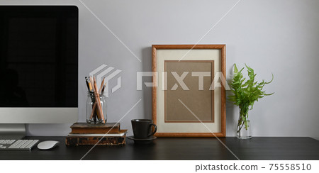 Photo of black working desk along with black blank screen computer monitor, books, notebook, pencil holder, picture frame, potted plant putting together on it with white cement wall as background. Photo of black working desk along with black blank screen computer monitor, books, notebook, pencil holder, picture frame, potted plant putting together on it with white cement wall as background. 75558510