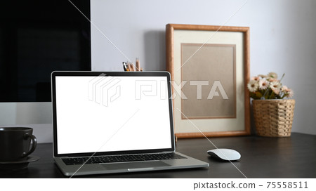 Photo of black working desk along with white blank screen computer laptop, books, notebook, pencil holder, picture frame, potted plant putting together on it with white cement wall as background. Photo of black working desk along with white blank screen computer laptop, books, notebook, pencil holder, picture frame, potted plant putting together on it with white cement wall as background. 75558511