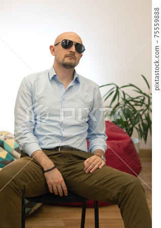 Baldheaded bearded brutal man in sunglasses sitting on chair Baldheaded bearded brutal man in sunglasses sitting on chair 75559888