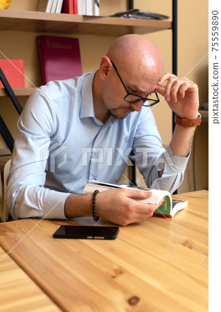 concentrated bald bearded man reading book in library 75559890