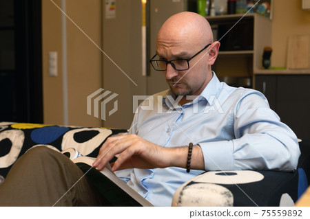 Man reading book at home sitting on couch in modern living room. pastime 75559892