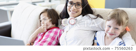 Smiling woman is sitting on sofa with girls. Smiling woman is sitting on sofa with girls. 75560263