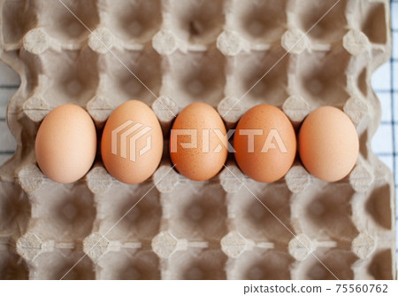 Several brown eggs lie in a row in a large cardboard storage bag Several brown eggs lie in a row in a large cardboard storage bag 75560762