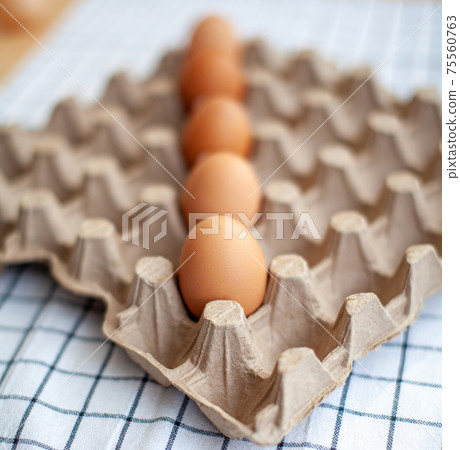 Several brown eggs lie in a row in a large cardboard storage bag Several brown eggs lie in a row in a large cardboard storage bag 75560763
