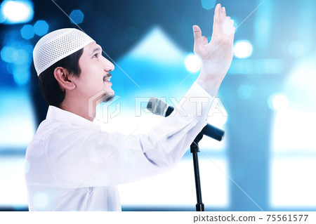 Asian Muslim man standing while raised hands and giving a sermon 75561577