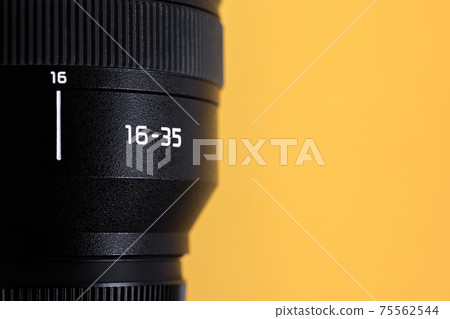 Professional wide angle photo lens with focal distance 16-35mm at yellow background with copy space Professional wide angle photo lens with focal distance 16-35mm at yellow background with copy space 75562544