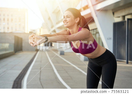 Smiling sportswoman stretching early in the morning outdoor 75563121