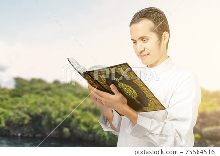Asian Muslim man standing and reading the Quran 75564516