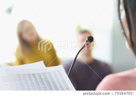 Woman in front of microphone reading information from paper closeup 75564705