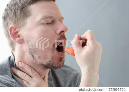 Young man holding his neck and inhaling medicine from inhaler 75564721