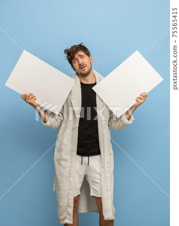 Caucasian man in white bathrobe with sheets of paper isolated on blue background Caucasian man in white bathrobe with sheets of paper isolated on blue background 75565415