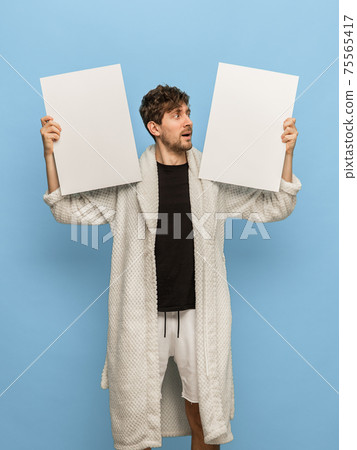 Caucasian man in white bathrobe with sheets of paper isolated on blue background Caucasian man in white bathrobe with sheets of paper isolated on blue background 75565417
