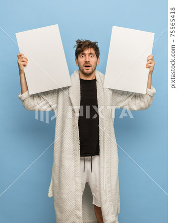 Sleepy man in white bathrobe with sheets of paper isolated on blue background Sleepy man in white bathrobe with sheets of paper isolated on blue background 75565418