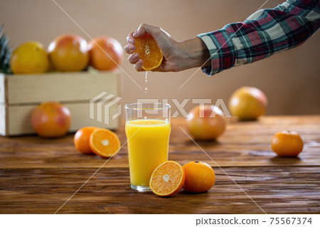 Female hand squeezing fresh orange to the glass on wood table Female hand squeezing fresh orange to the glass on wood table 75567374