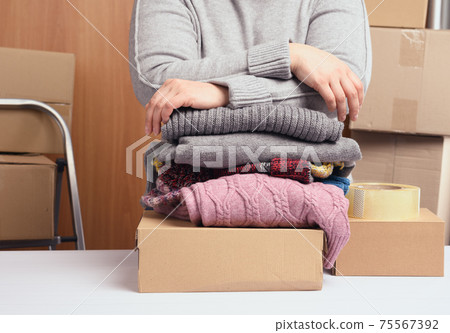 woman in a gray sweater is packing clothes in a box, the concept of assistance and volunteering, moving woman in a gray sweater is packing clothes in a box, the concept of assistance and volunteering, moving 75567392