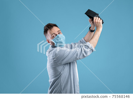 Desperate Caucasian man in protective mask shaking empty wallet, having no money during covid on blue background Desperate Caucasian man in protective mask shaking empty wallet, having no money during covid on blue background 75568146