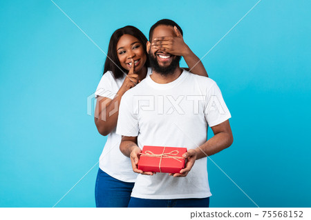 Happy black woman making surprise for her boyfriend giving box 75568152
