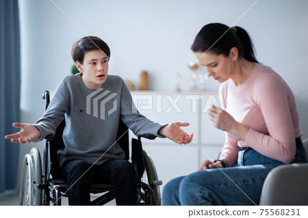 Family disagreement. Upset mother crying and her teenage son in wheelchair trying to justify himself at home Family disagreement. Upset mother crying and her teenage son in wheelchair trying to justify himself at home 75568231