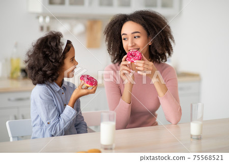 Black mother and daughter eating sweets in kitchen Black mother and daughter eating sweets in kitchen 75568521