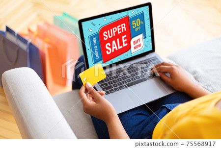 Black woman using laptop and credit card at home 75568917