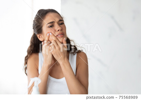 Frustrated Lady With Acne Problem Squeezing Pimple On Cheek Indoor 75568989