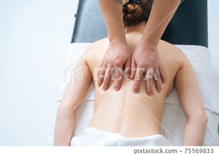 Top close-up view of male masseur massaging back and shoulders of female lying on massage table Top close-up view of male masseur massaging back and shoulders of female lying on massage table 75569833