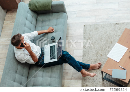 young man is talking on a smartphone, sitting on the sofa. young man is talking on a smartphone, sitting on the sofa. 75569834