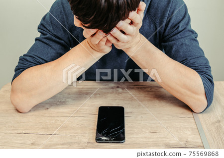 frustrated young man looking at his broken smartphone. frustrated young man looking at his broken smartphone. 75569868