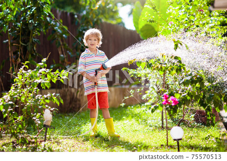 Boy watering flower in garden. Kid with water hose 75570513