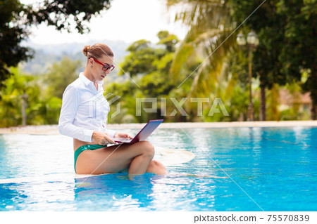 Woman with laptop at swimming pool. Remote work. 75570839