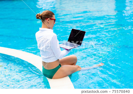 Woman with laptop at swimming pool. Remote work. 75570840