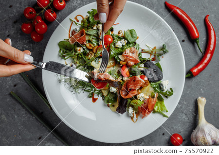 jamon salad, salad mix, spinach, pear, cherry tomatoes, Dor Blue, capers and vinegar dressing Bianco. Female hands holds fork and knife jamon salad, salad mix, spinach, pear, cherry tomatoes, Dor Blue, capers and vinegar dressing Bianco. Female hands holds fork and knife 75570922