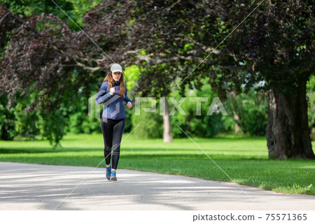 Young woman jogging in park on sunny day Young woman jogging in park on sunny day 75571365