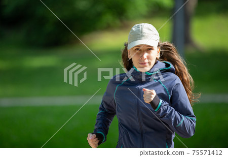 Portrait of woman jogging in park on sunny day 75571412