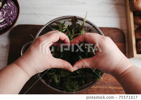 Woman making heart sign on green salad background 75571817