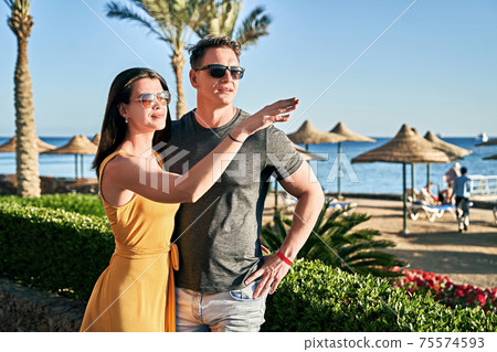 Beautiful caucasian couple on sea vacation in a tropical resort. Woman is pointing at something interesting on the horizon. 75574593