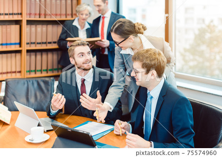 Lawyers in their law firm working on computer with books in background Lawyers in their law firm working on computer with books in background 75574960