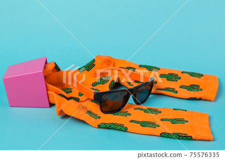 two orange socks with a pattern of green cacti, lie on a turquoise background, as if growing from a flowerpot, next to them are sunglasses, travel concept 75576335