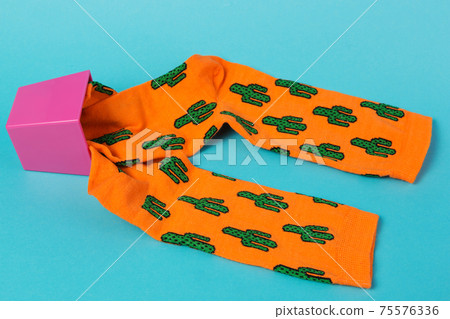 two orange socks with a pattern of cacti, lie on a turquoise background, as if growing out of a flowerpot, the flowerpot overturned, concept 75576336
