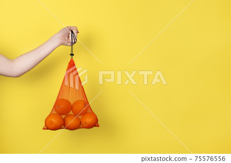 Female hand holding Oranges in eco bag for grocery isolated on yellow. Eco friendly Shopping Bag concept. Banner with copy space. Female hand holding Oranges in eco bag for grocery isolated on yellow. Eco friendly Shopping Bag concept. Banner with copy space. 75576556